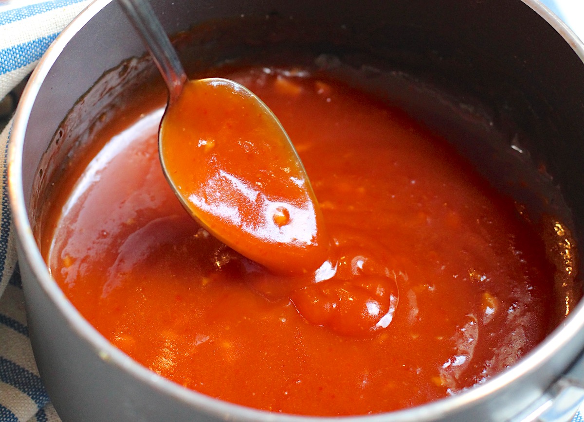 Spoon scooping Honey Sriracha Sauce in the pot.
