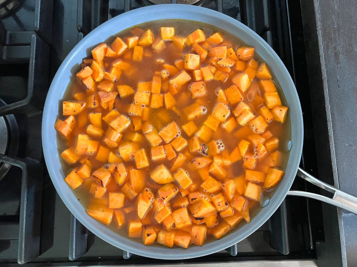Diced sweet potatoes in a skillet with stock covering the potatoes.