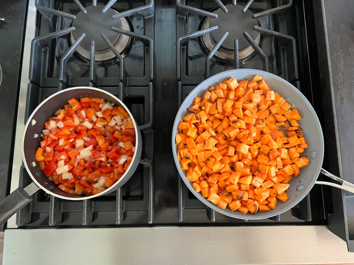 Saucepan with onions and red peppers and a skillet filled with diced sweet potatoes on a stove.