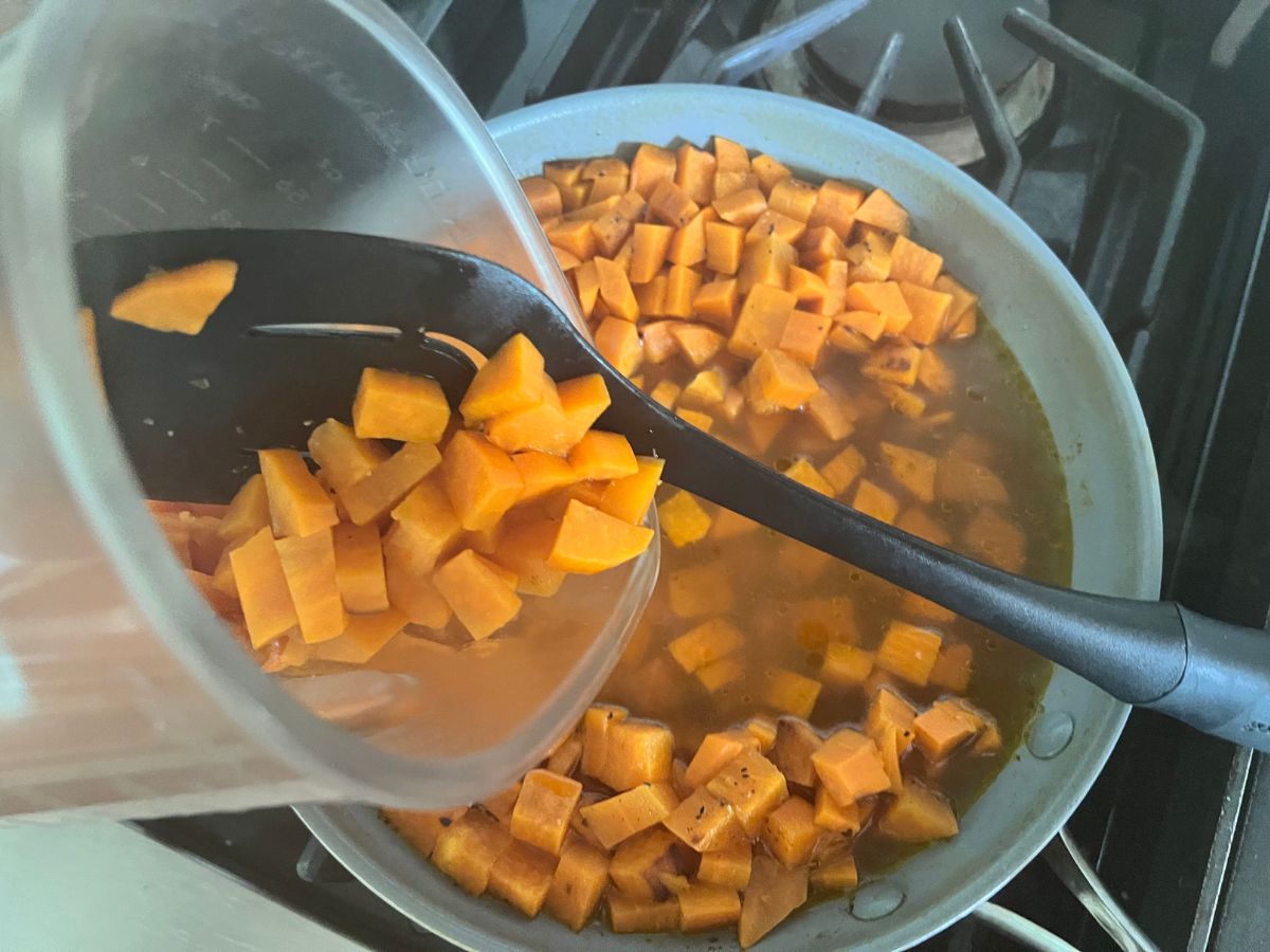 Cooked diced sweet potatoes being strained from the stock and added to a blender.