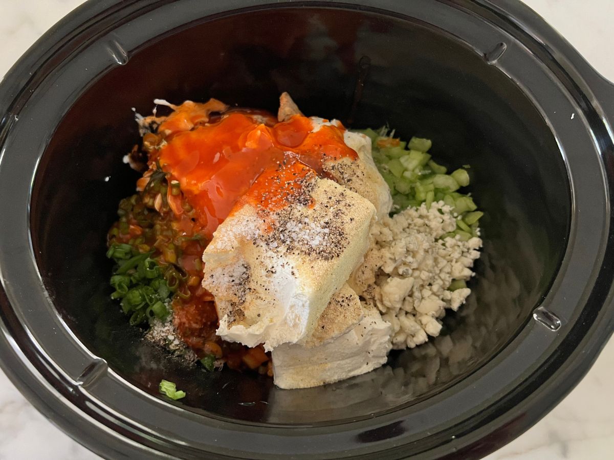 Buffalo sauce added to cream cheese mixture in a slow cooker.