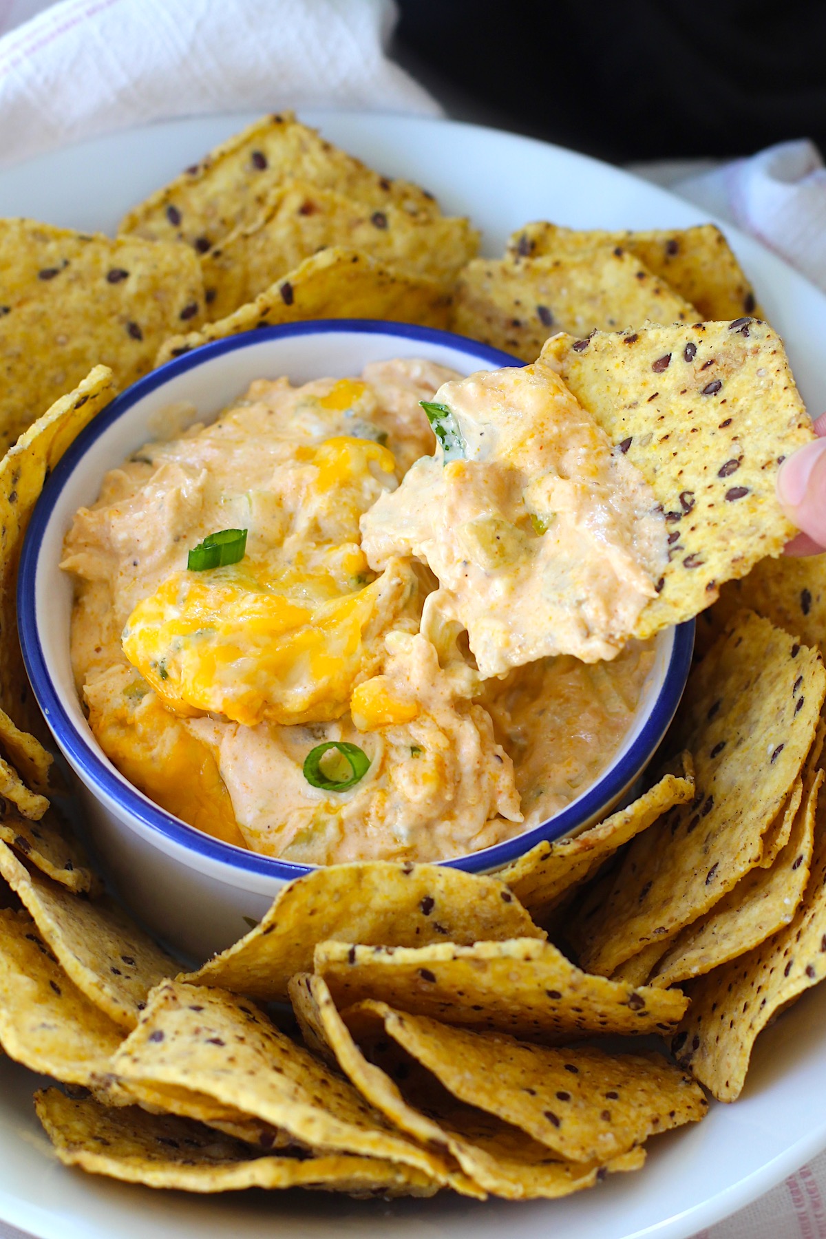Slow cooker Chicken Buffalo Dip in a serving bowl with sliced scallions on top, tortilla chips all around the outside in another bowl, and a chip scooping dip from the bowl.