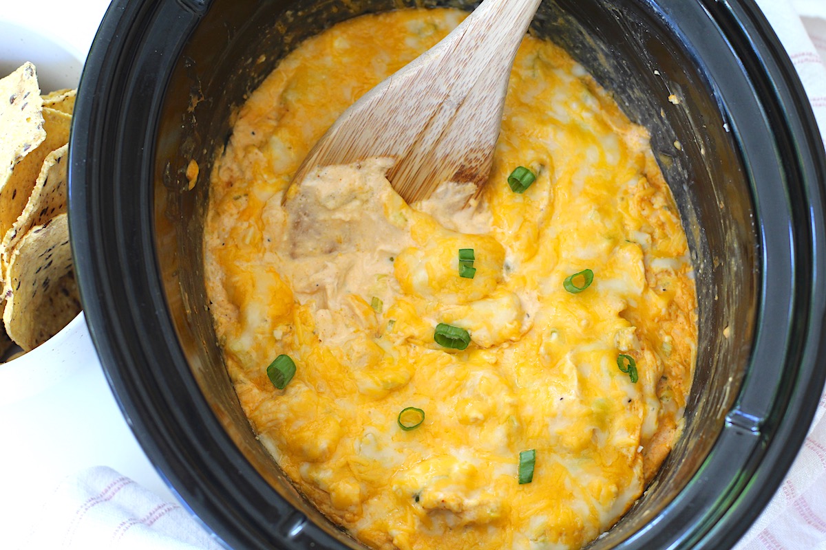 Slow cooker Chicken Buffalo Dip in crock pot inset with wood spoon scooping through the top layer of melty cheese.