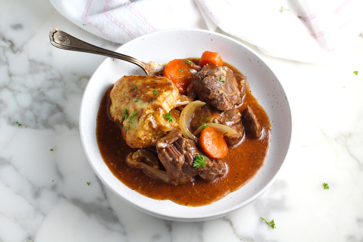 Dumpling in a bowl with carrots and onions and a fork on marble counter. Parsley sprinkled on top.
