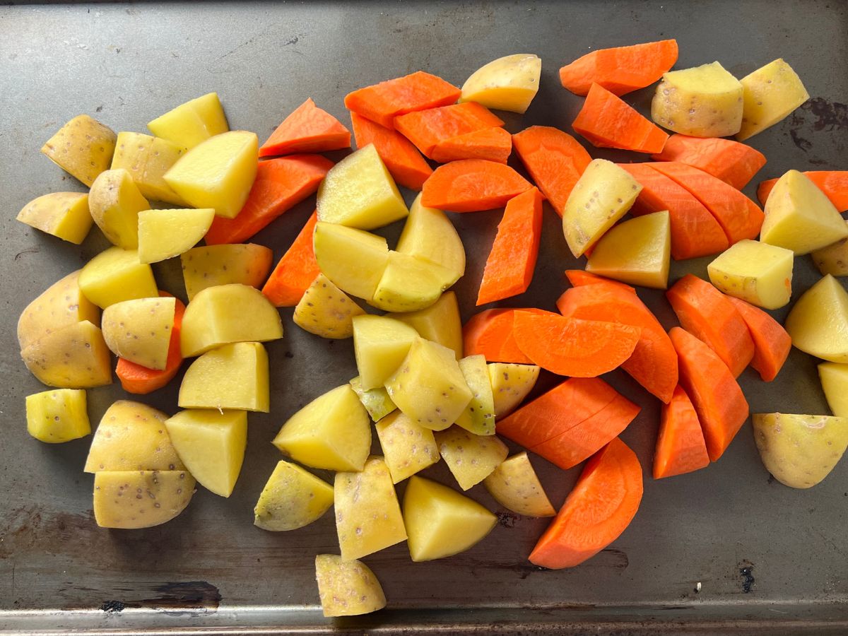 Potatoes and carrots cut up and laying on a baking sheet.