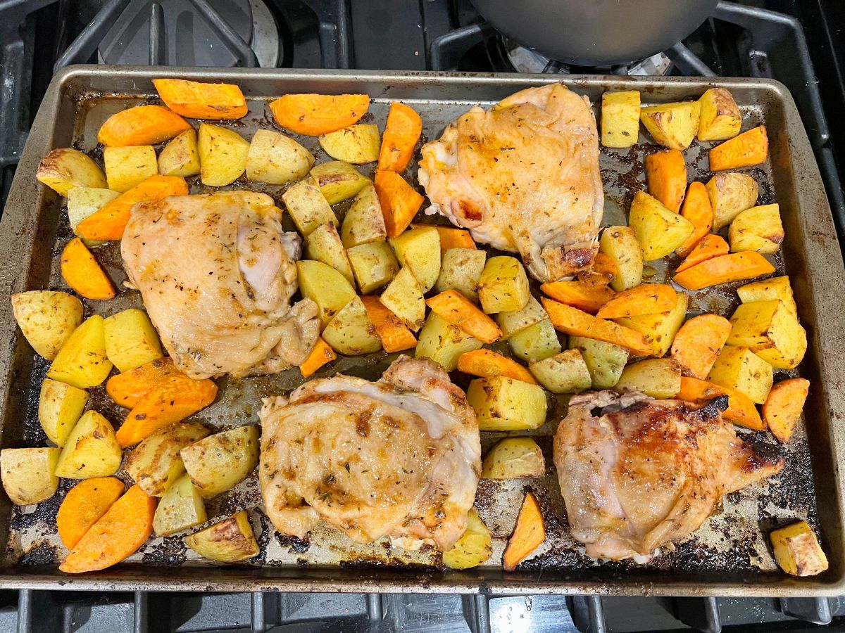 Baked chicken thighs, carrots and potatoes on a baking tray, ready to serve.
