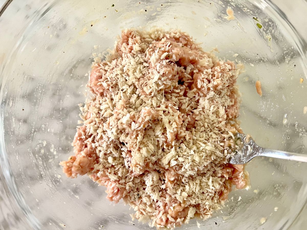 Breadcrumbs added to a ground chicken mixture in a mixing bowl.