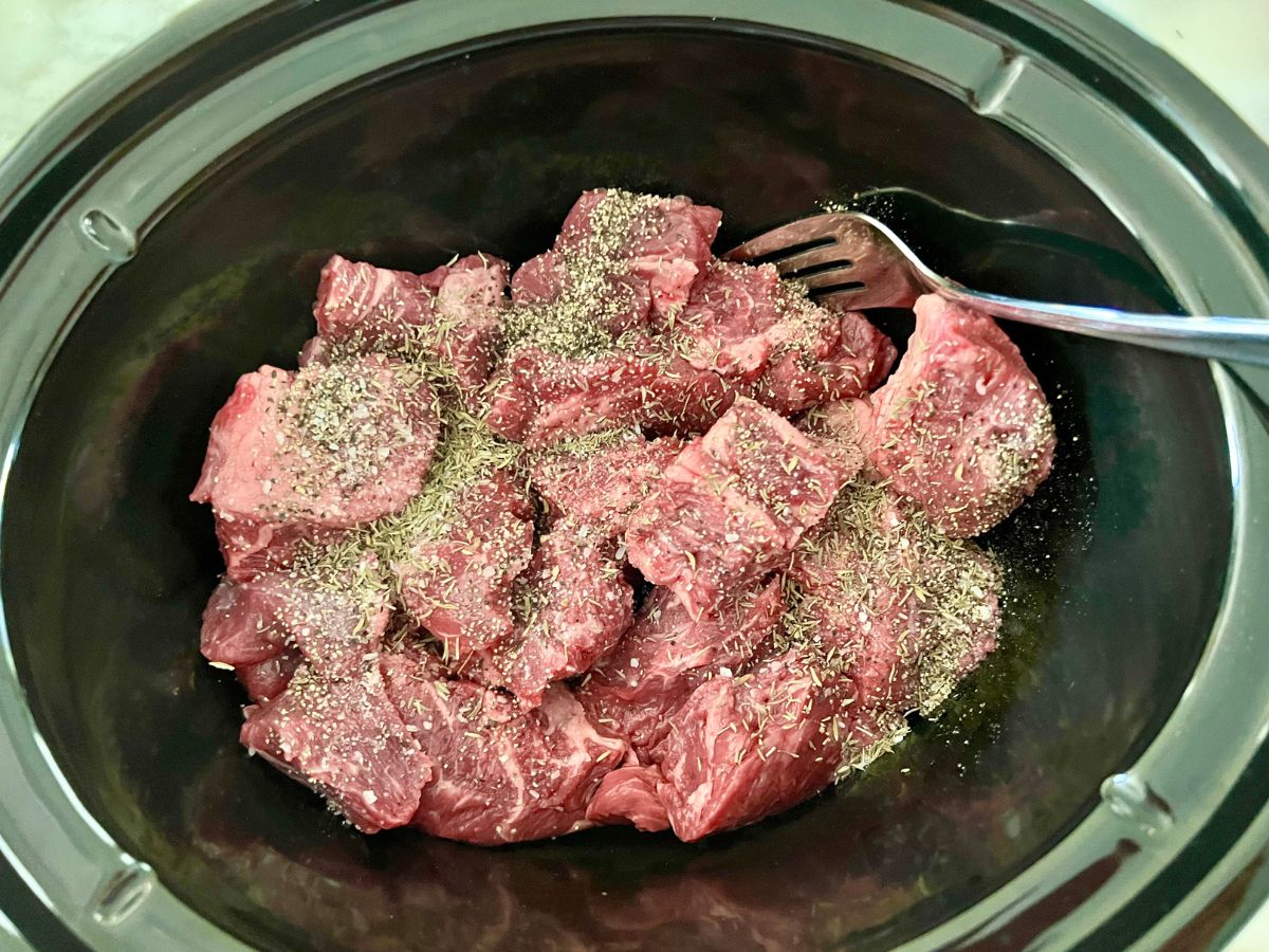 Beef stew meat and seasonings added to the slow cooker.