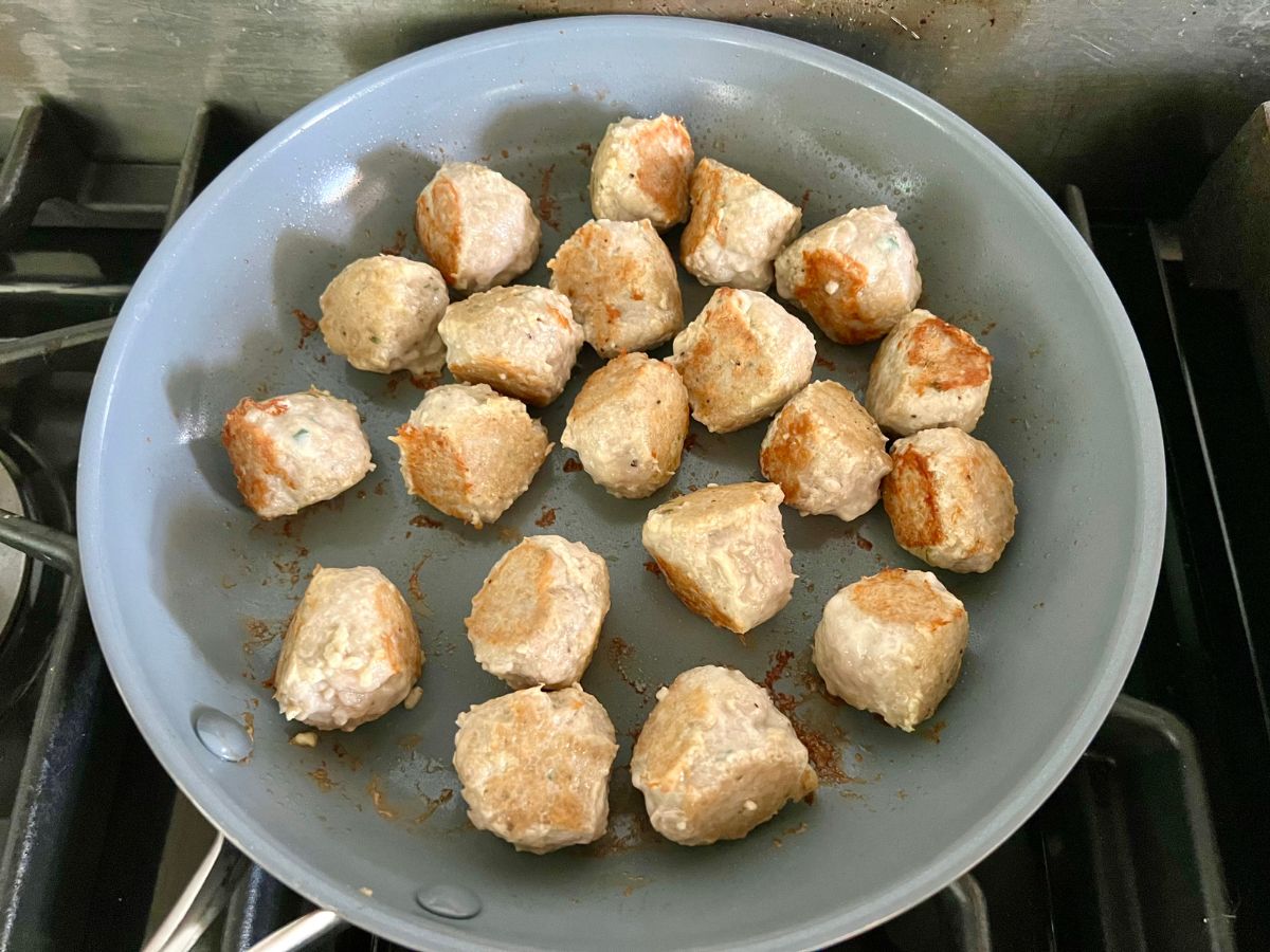 Browning chicken meatballs in a skillet.
