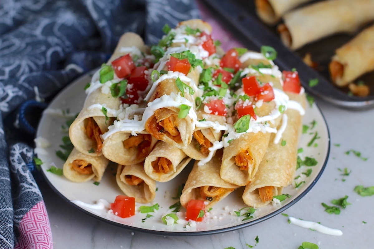 Taco Seasoning for Chicken recipe used on shredded chicken that's been added to rolled, baked, and stacked Taquitos topped with sour cream, tomatoes, and cilantro.