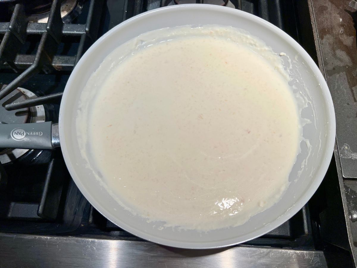 Alfredo sauce thickening in a skillet on the stove.