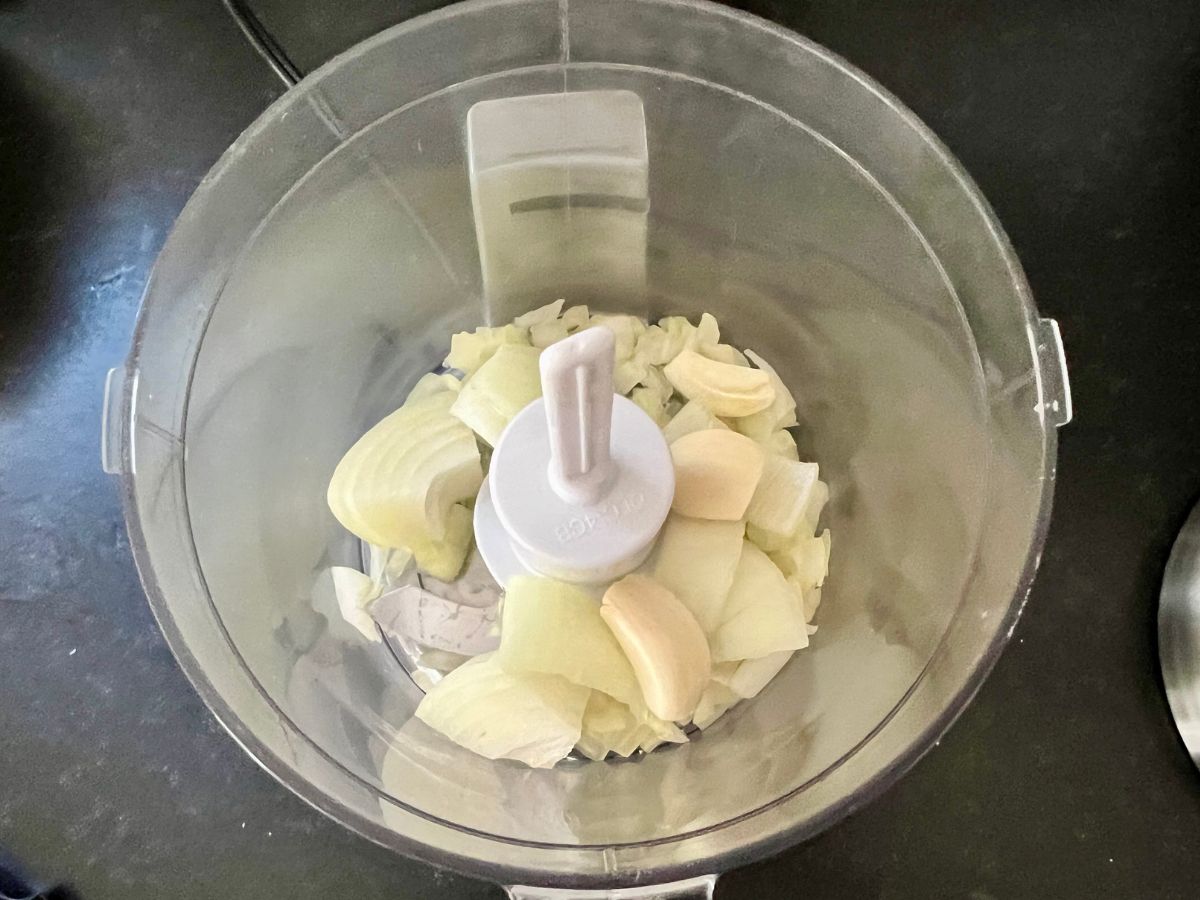 Food processor with chunks of onion and whole garlic cloves added.