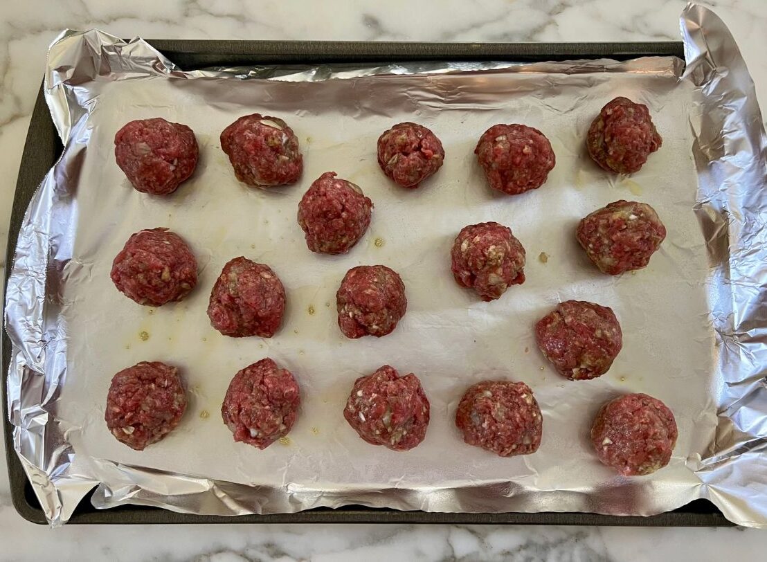 Ground beef meatball mixture scooped up into balls and resting on a foil lined baking sheet.