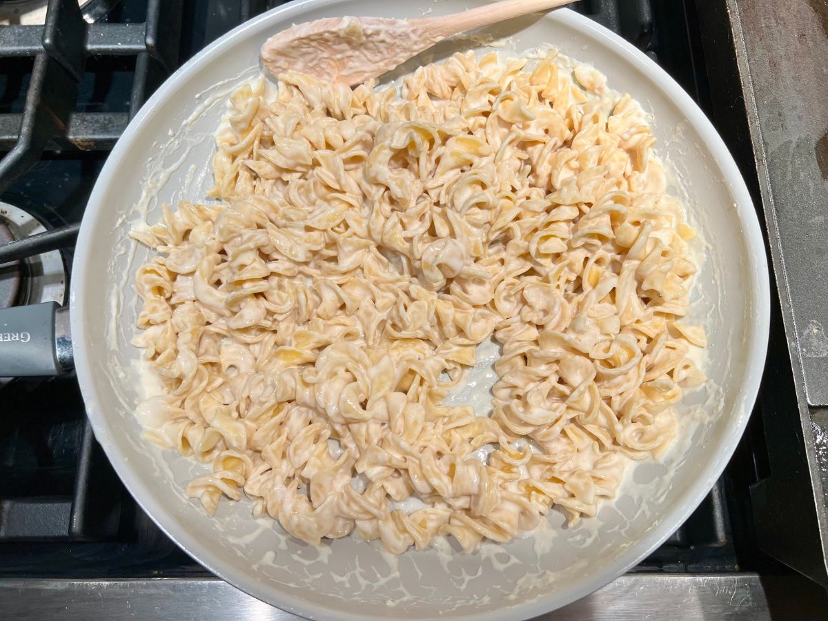 Pasta noodles combined with alfredo sauce in the skillet.