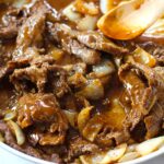 Black Pepper Beef Stir Fry with onions in a pan with wooden spoon.