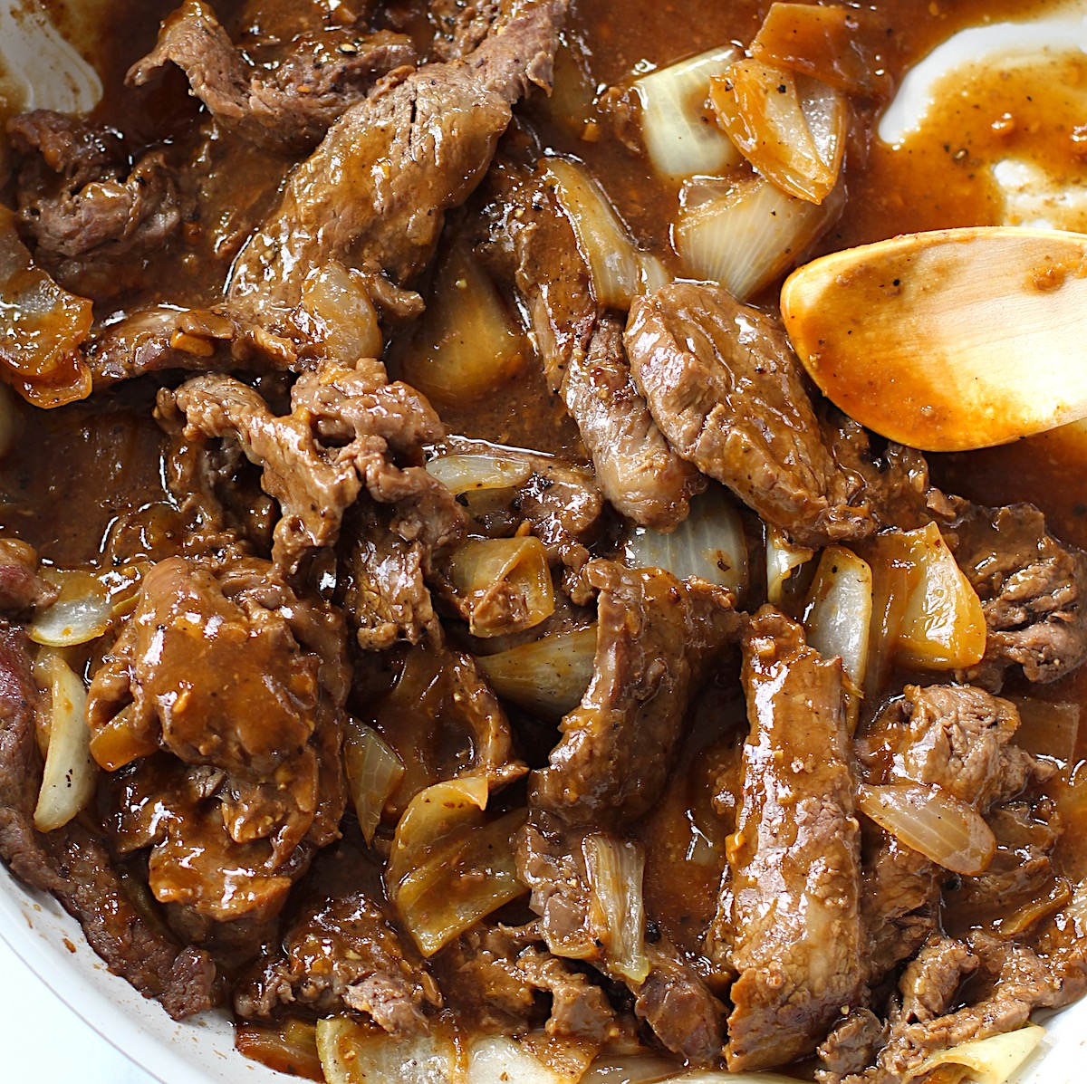 Black Pepper Beef Stir Fry with onions in a pan with wooden spoon.