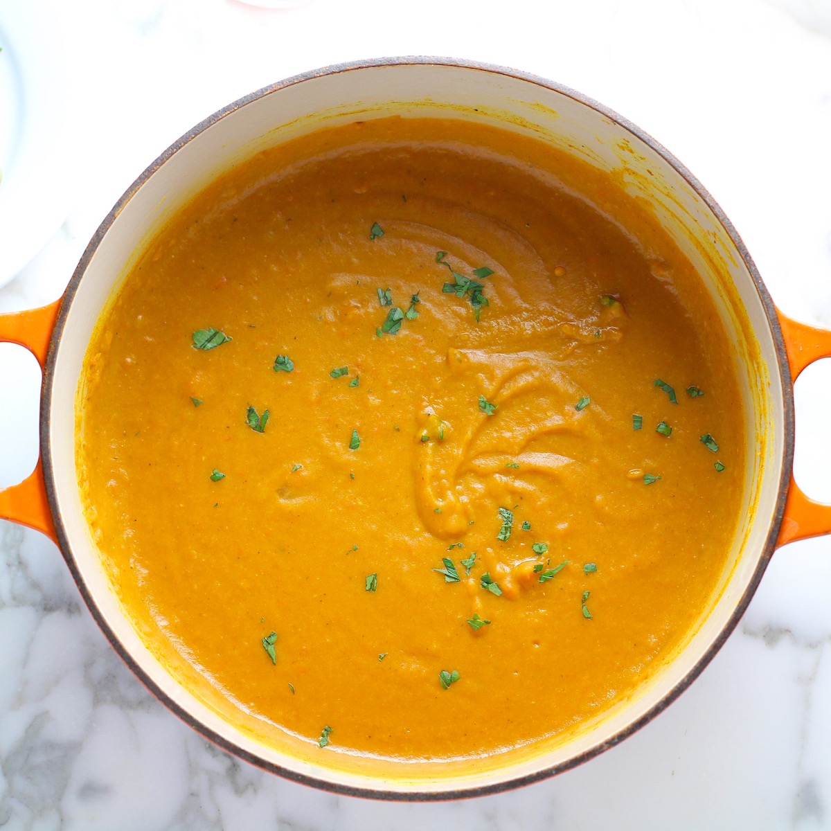 Creamy Carrot and Lentil Soup blended smooth in a pot on counter garnished with parsley.