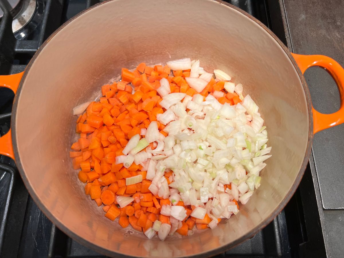 Diced onions and carrots added to a Dutch oven with garlic to saute.