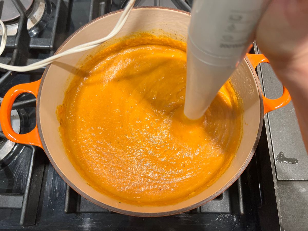 Immersion blender in the carrot and lentil mixture to create a smooth soup texture.