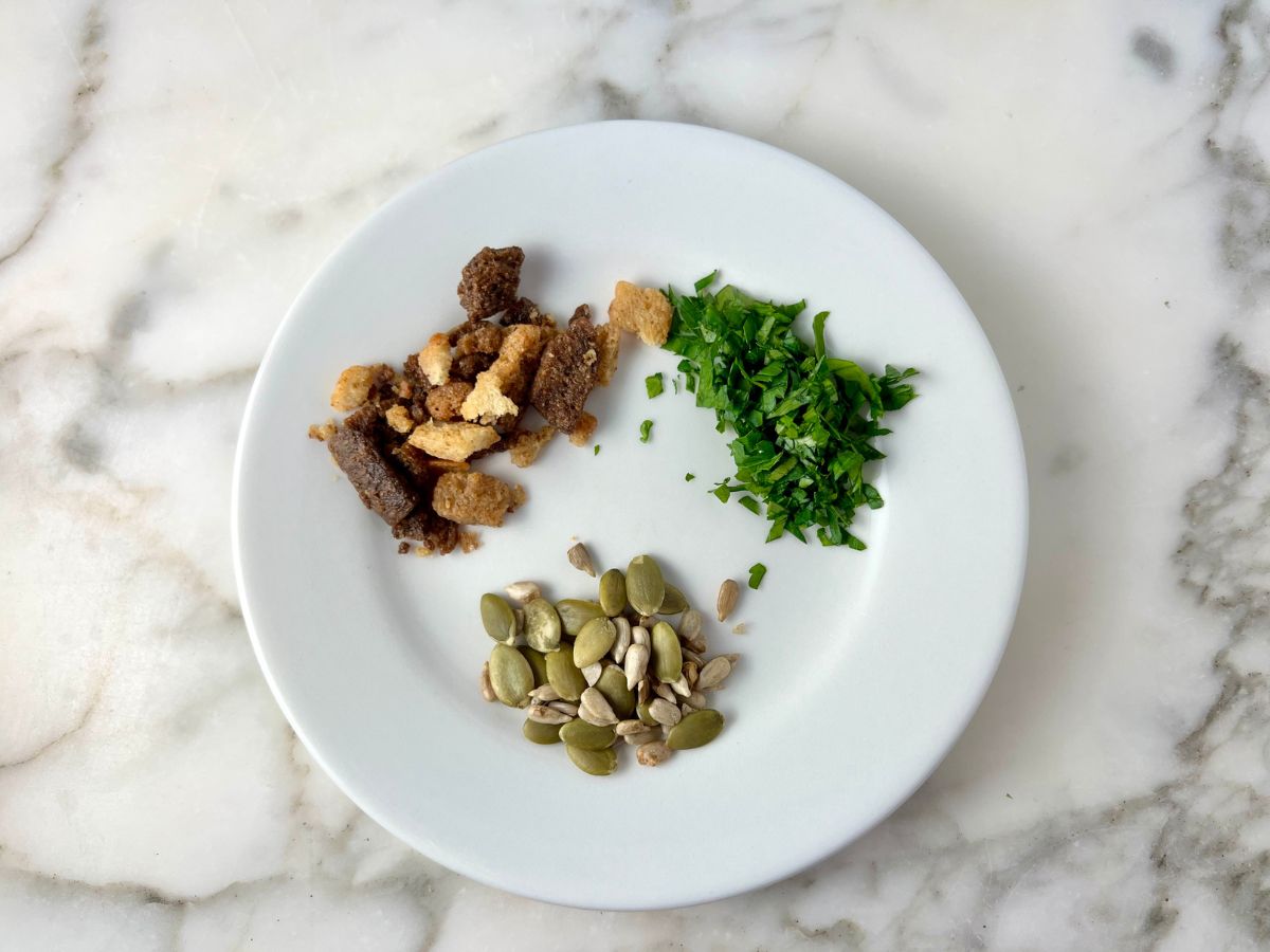 Pumpkin seeds, chopped parsley and croutons on a plate to use as a garnish for the soup.