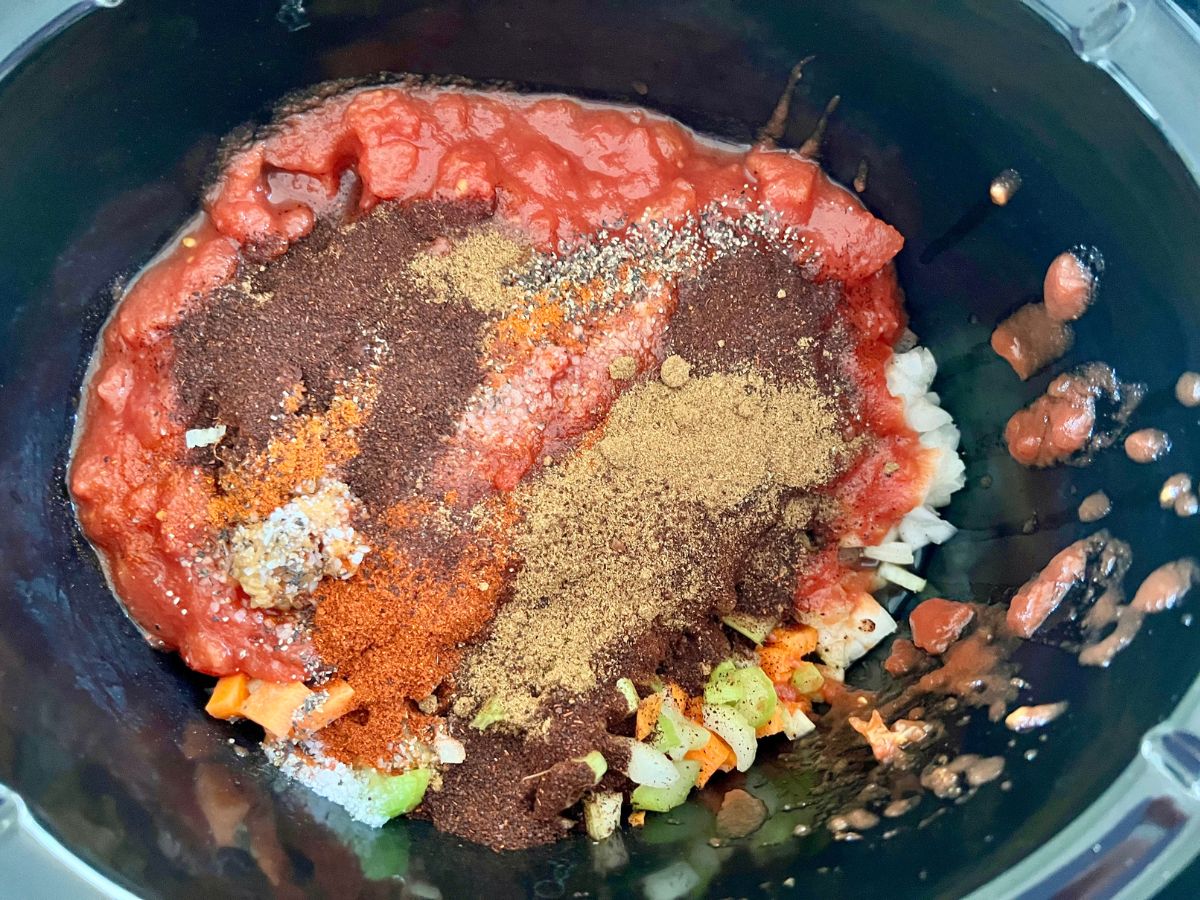 Slow cooker with diced tomatoes, seasonings, veggies added to it.