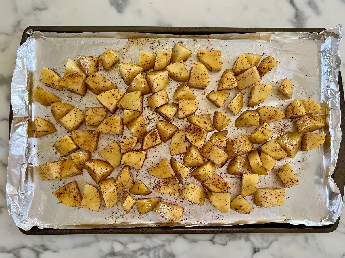 Diced potatoes pieces coated in oil and seasonings and placed in a single layer on an aluminum foil coated baking sheet.