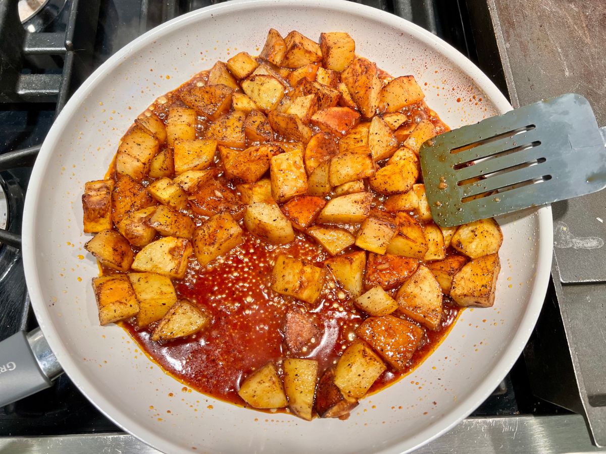 Honey chili sauce added to the potatoes in a skillet.
