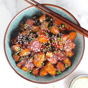 Honey Chilli Potatoes Recipe with sesame seeds and chives on top in a bowl with wood chopsticks.