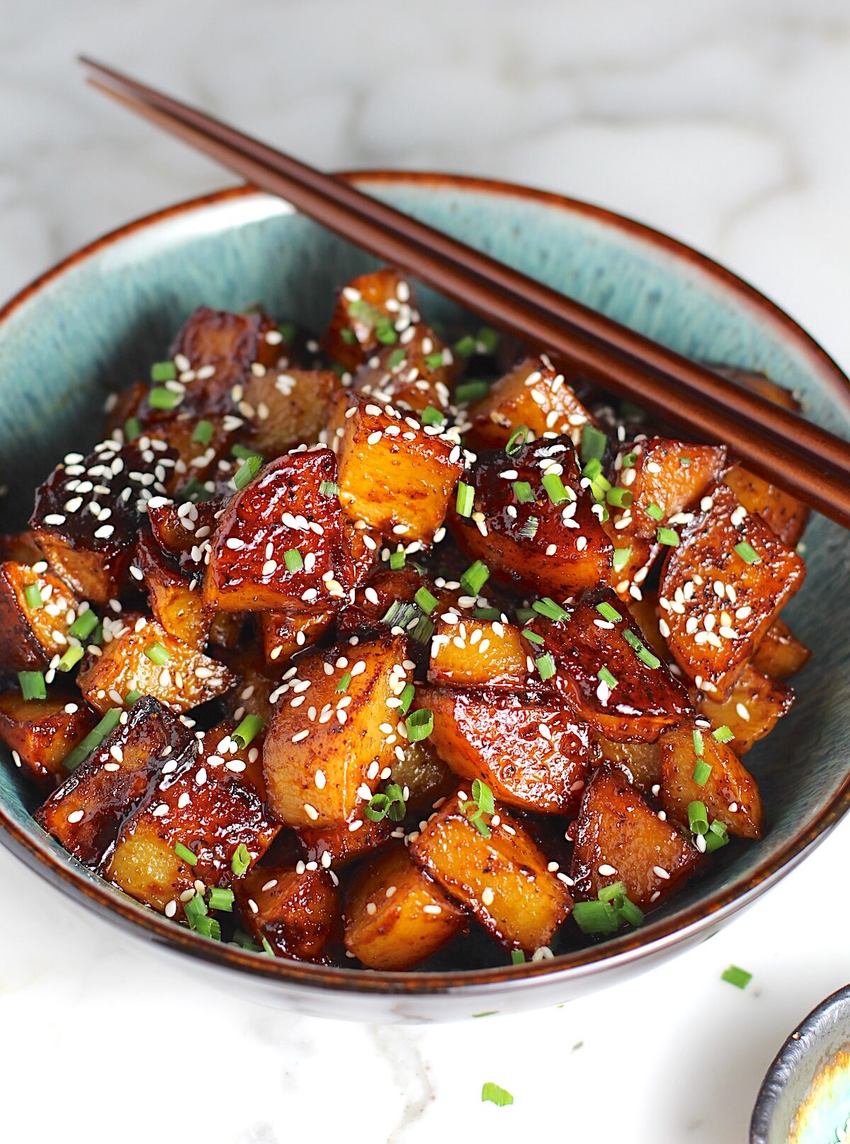 Honey Chilli Potatoes Recipe with sesame seeds and chives on top in a bowl with wood chopsticks.