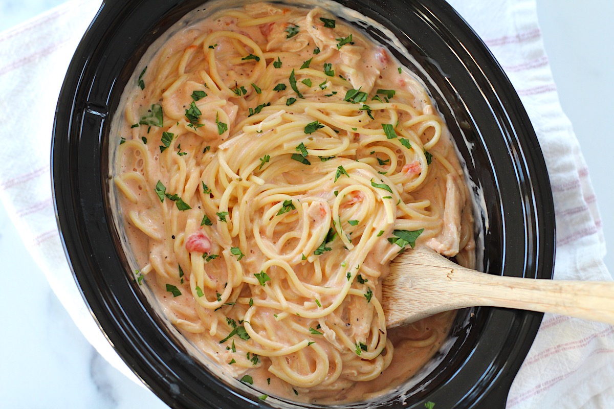 Slow Cooker Chicken and Spaghetti in a creamy cheesy sauce in a slow cooker pot with wooden spoon.