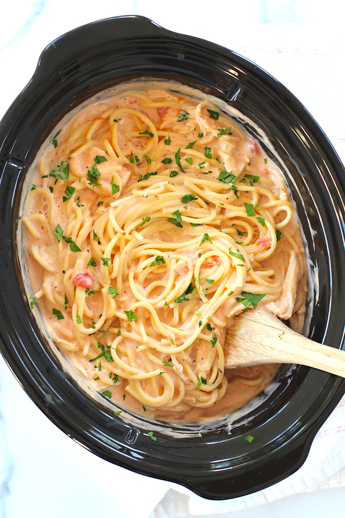 Slow Cooker Chicken and Spaghetti in a creamy cheesy sauce in a slow cooker pot with wooden spoon.