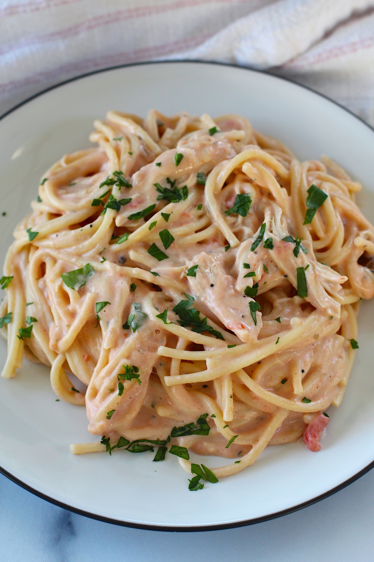 Slow Cooker Chicken and Spaghetti in a creamy cheesy sauce on a plate on a marble counter.
