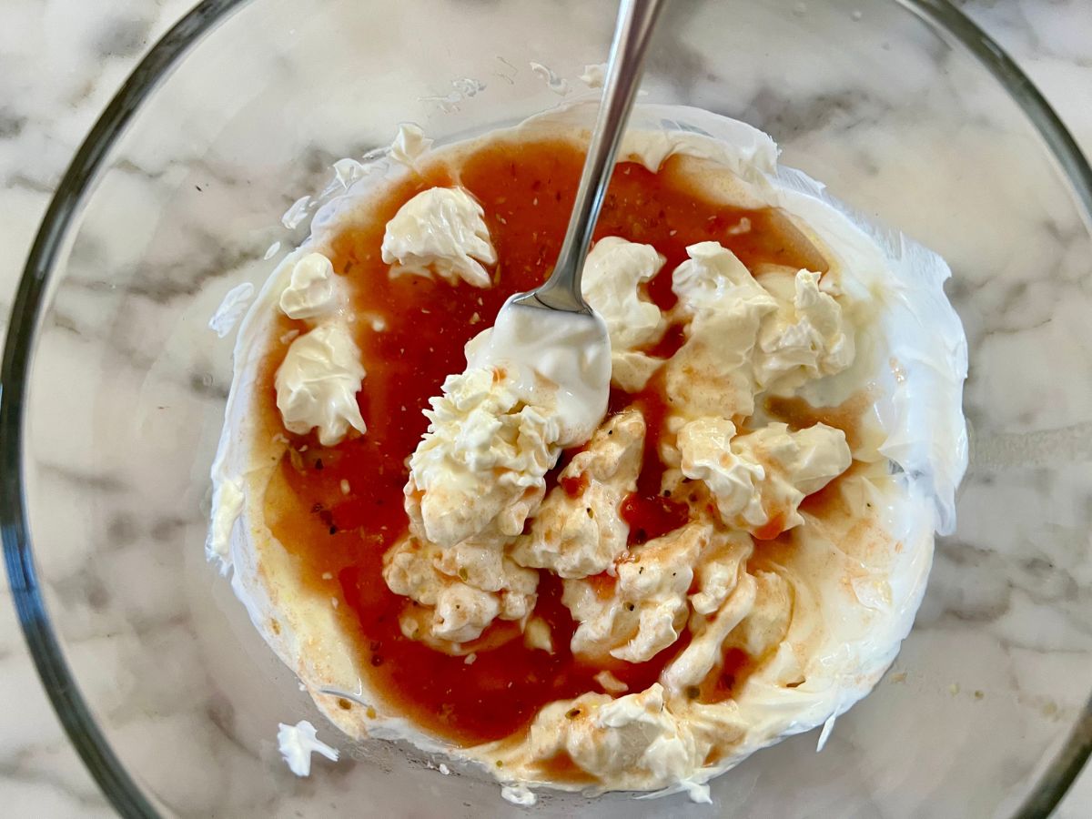 Fork combining sour cream, cornstarch, cream cheese and tomato mixture together in a mixing bowl.