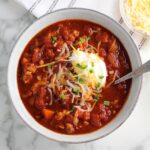 Chicken Chili with Ground Chicken in a bowl with a spoon, topped with sour cream, shredded cheese, and scallions.