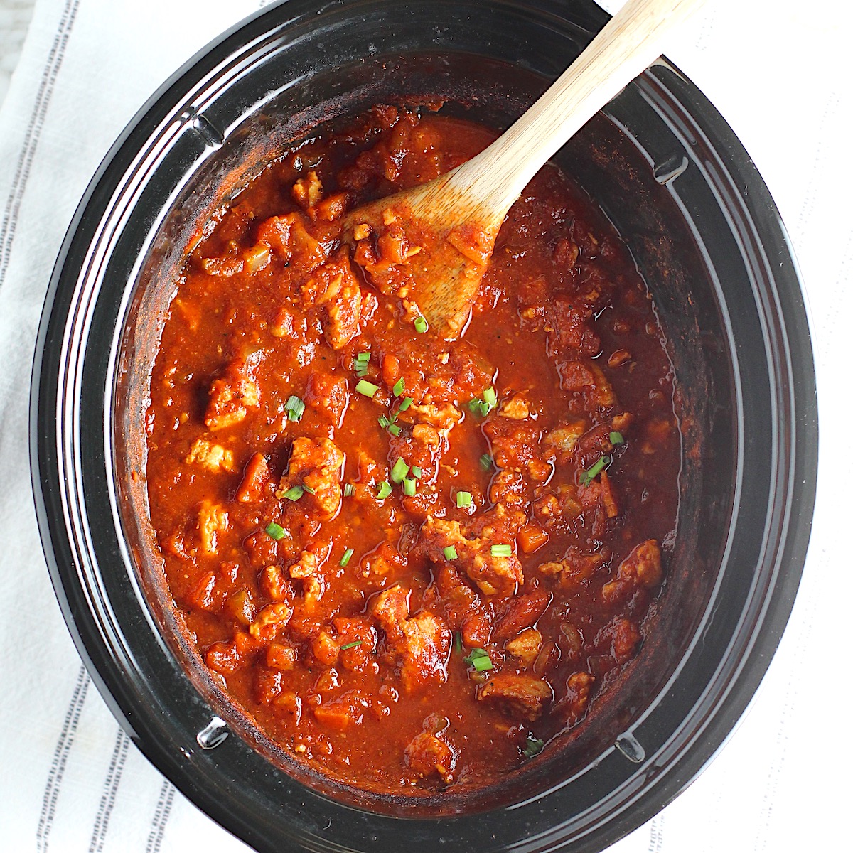 Chicken Chili with Ground Chicken in a slow cooker pot with a wooden spoon and garnished with scallions.