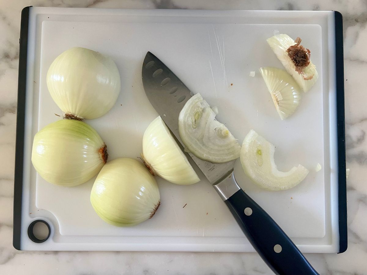 Chef's knife resting on some thinly sliced onions on a cutting board.