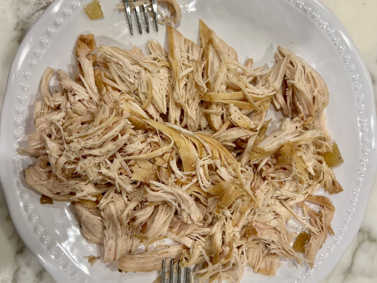 Two forks resting on a plate of shredded chicken.