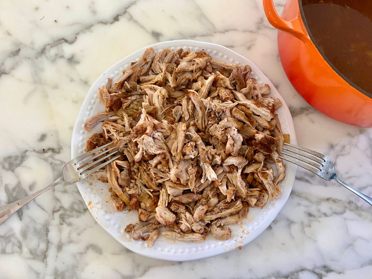 Pulled chicken thighs on a plate shredded to small pieces with two forks resting on the edges.
