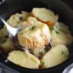 Serving spoon scooping up slice of baguette with melty cheese pulls from the Chicken French Onion Soup Slow Cooker recipe.