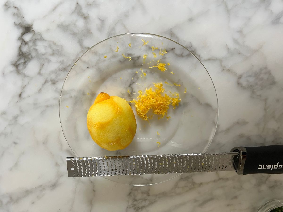 Zester resting on a plate with lemon zested by the lemon.