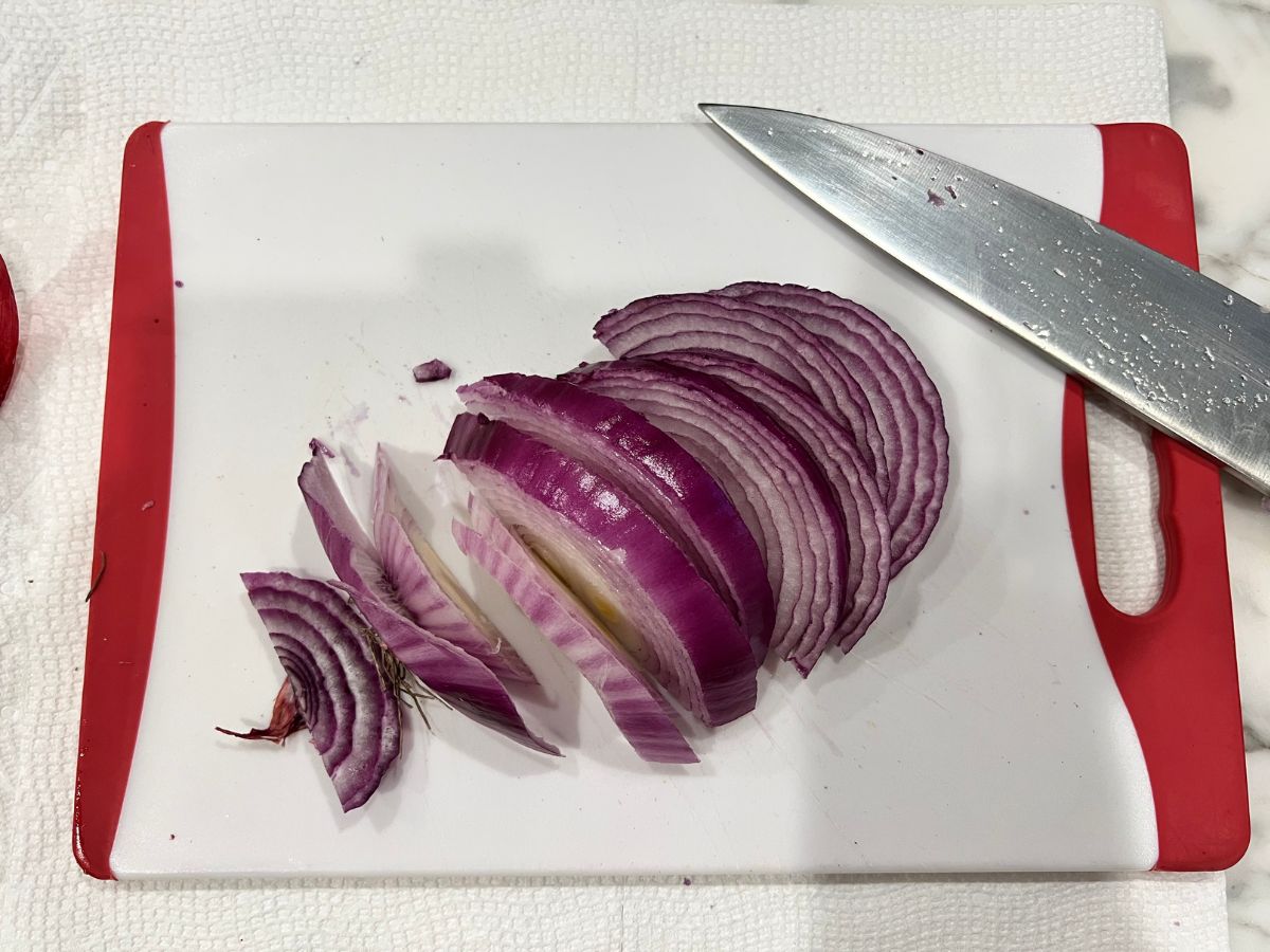 Red onion cut into thin sliced pieces on a cutting board with a chef's knife resting with it.