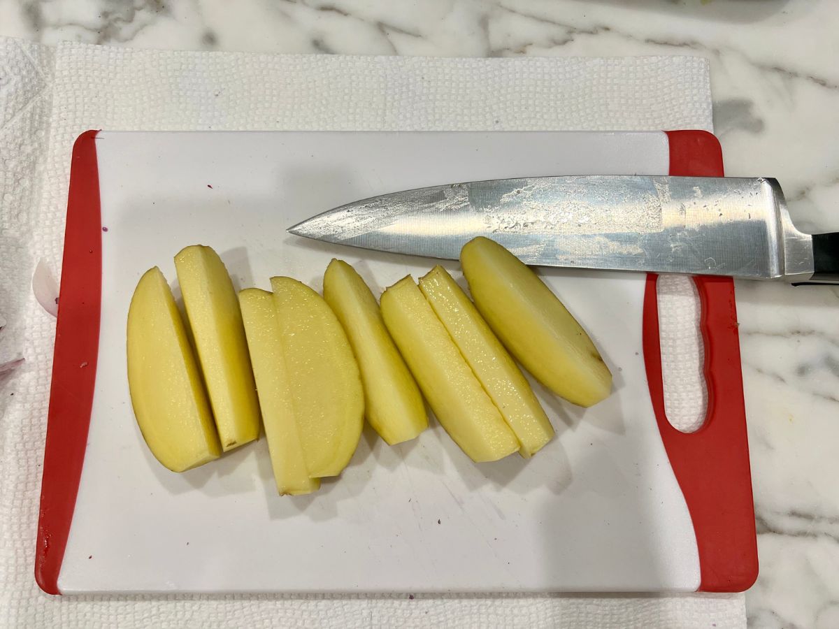 Sliced potatoes on a cutting board with a chef's knife resting on the edge.