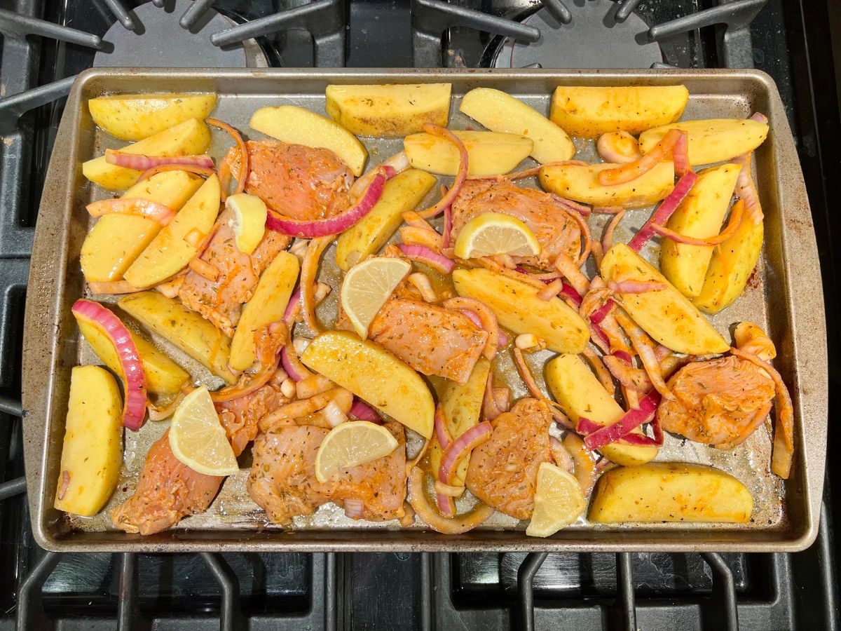 Marinated potatoes, chicken and onions on a baking sheet ready to bake.