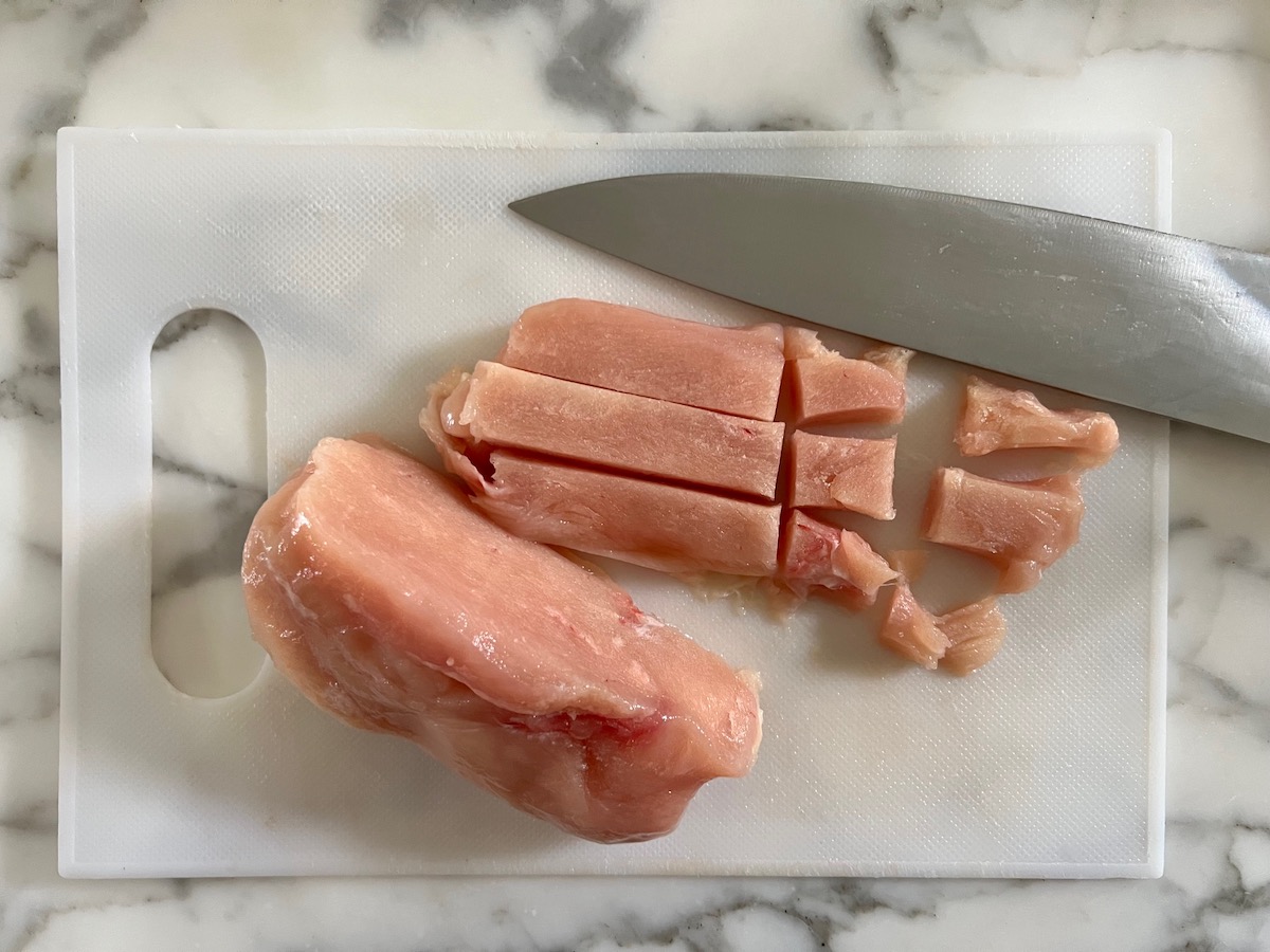 Semi-frozen chicken being cut into cubes on a cutting board for Chicken Chorizo Orzo.