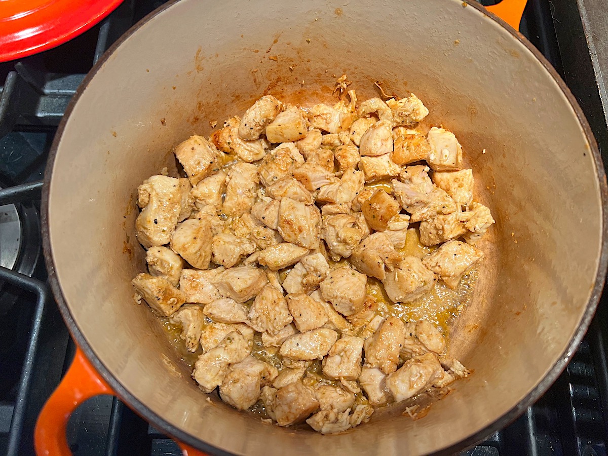Cubed chicken breast cooking in a pot on stove for Chicken Chorizo Orzo.