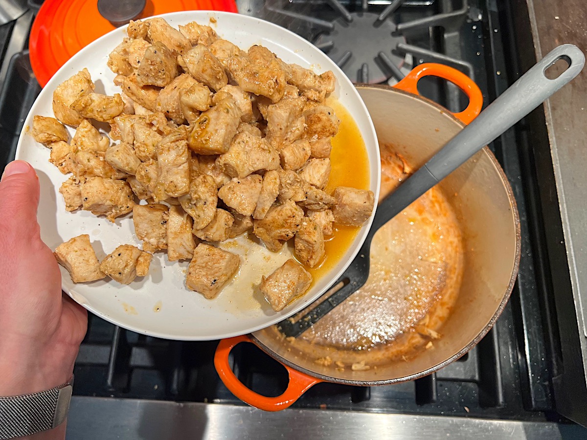 Cooked chicken breast pieces being transferred from the pot to the plate over stove for Chicken Chorizo Orzo.