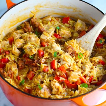 Creamy Chicken Chorizo Orzo dinner with red peppers in a dutch oven sitting on the counter with a wooden spoon scooping.
