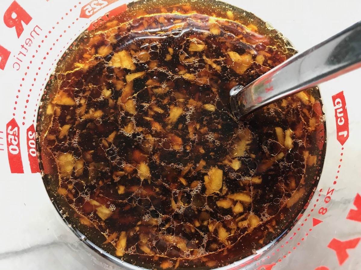 Measuring cup with soy sauce, honey sesame oil, minced garlic, and minced ginger being mixed on counter for Beef and Broccoli Noodles recipe.