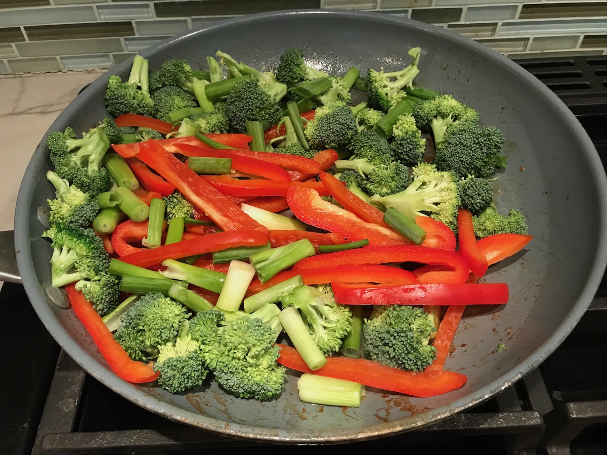 Broccoli florets, scallions, and red peppers stir frying in a pan for Beef and Broccoli Noodlle recipe.