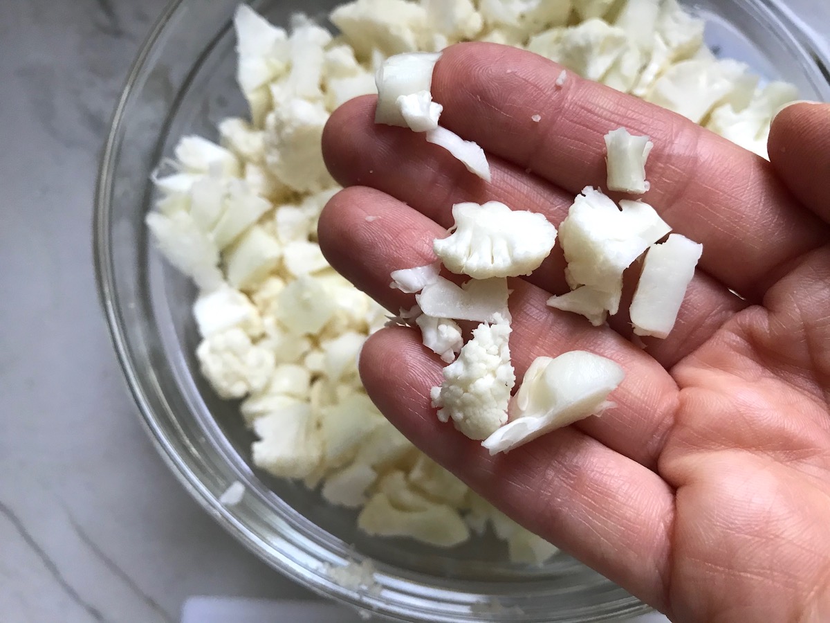 Hand holding small cauliflower pieces over a bowl of cauliflower to show the small size for Vegetarian Sloppy Joes Recipe.